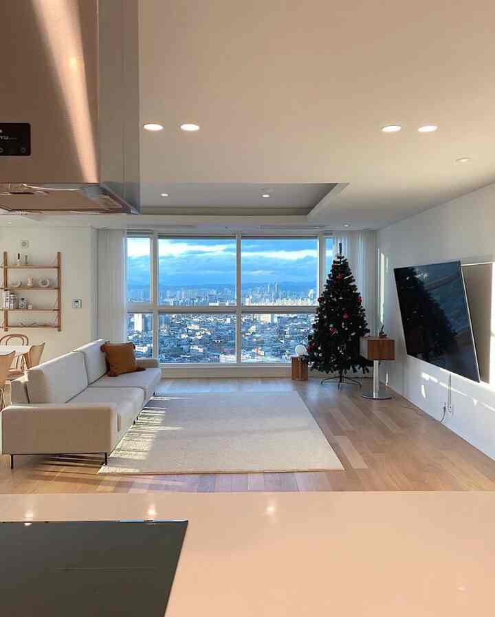 Bright and modern living room with white and wood tones, featuring a large window and decorated Christmas tree