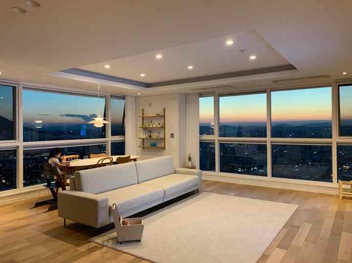 White and natural color toned living and dining room featuring bright fabric sofa, dining table, and large windows showcasing sunset view, cozy atmosphere