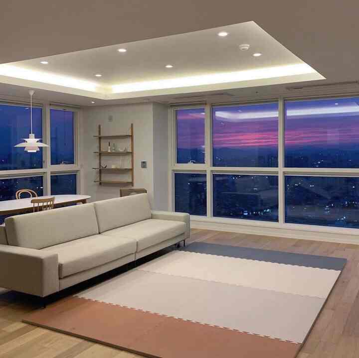 Natural brown and white toned living room featuring beige sofa, dining table, and puzzle play mat in a modern setting