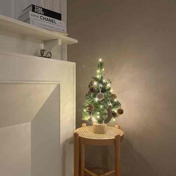 Natural-tone living room space featuring a mini Christmas tree on a round stool, decorative fireplace, and vintage candleholder creating a cozy atmosphere