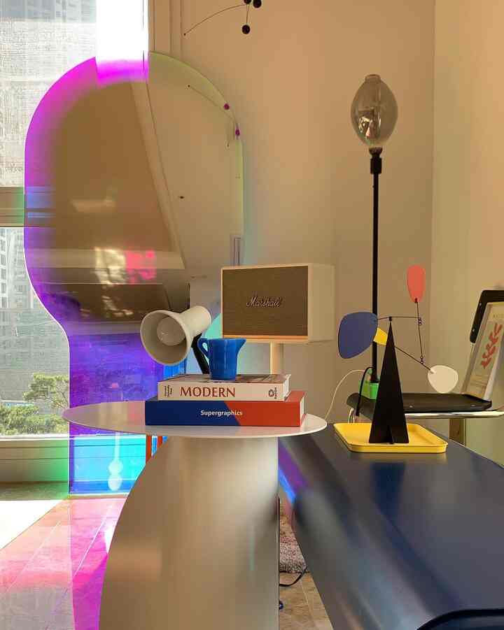 ホワイトのサイドテーブルとブルーのベンチがあるリビング、ホログラムの全身鏡とレトロ照明が印象的な空間を作る