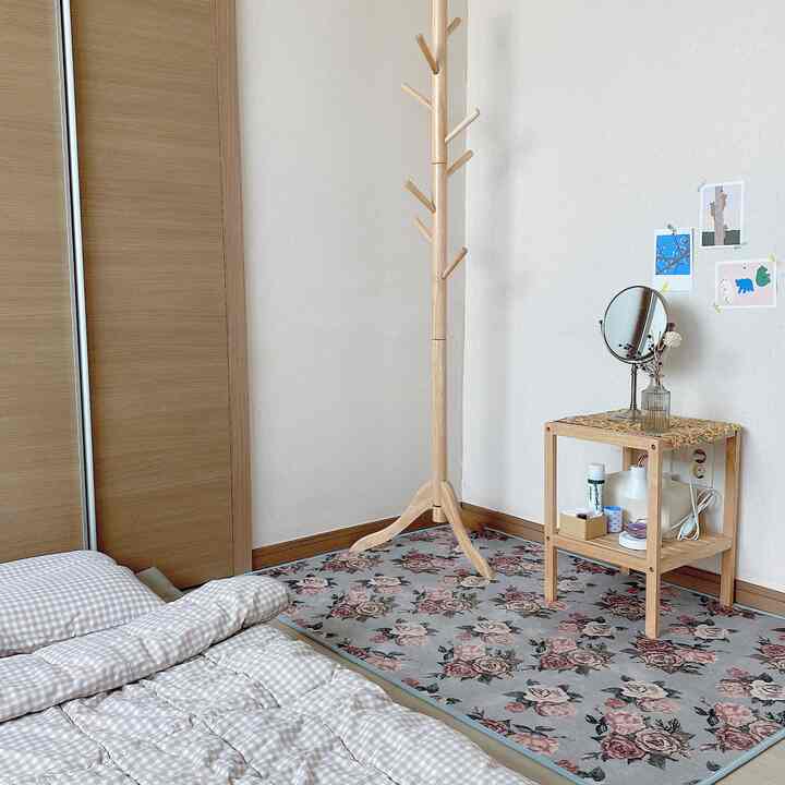 ベージュ調のゲストルーム、木製ハンガースタンドと花柄のローズラグ、化粧台が配置された雰囲気のあるインテリア