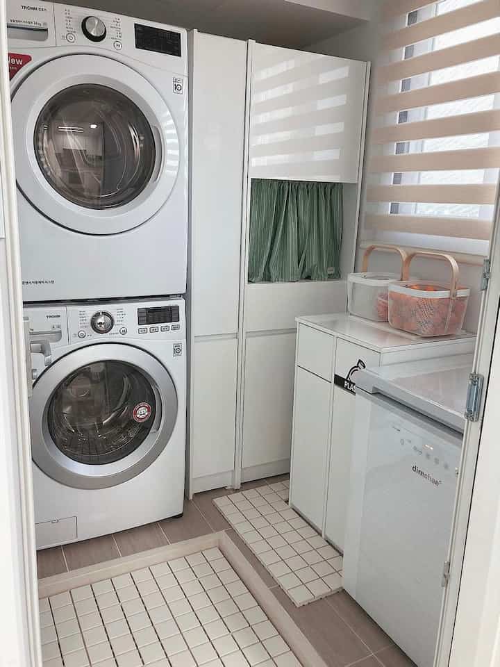 White-toned utility room featuring stacked washer and dryer, storage cabinets, and a tension rod partition with a clean layout