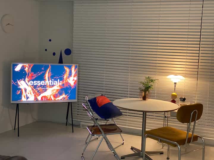 White-toned living room featuring round dining table, blinds, and table lamp creating a cozy atmosphere