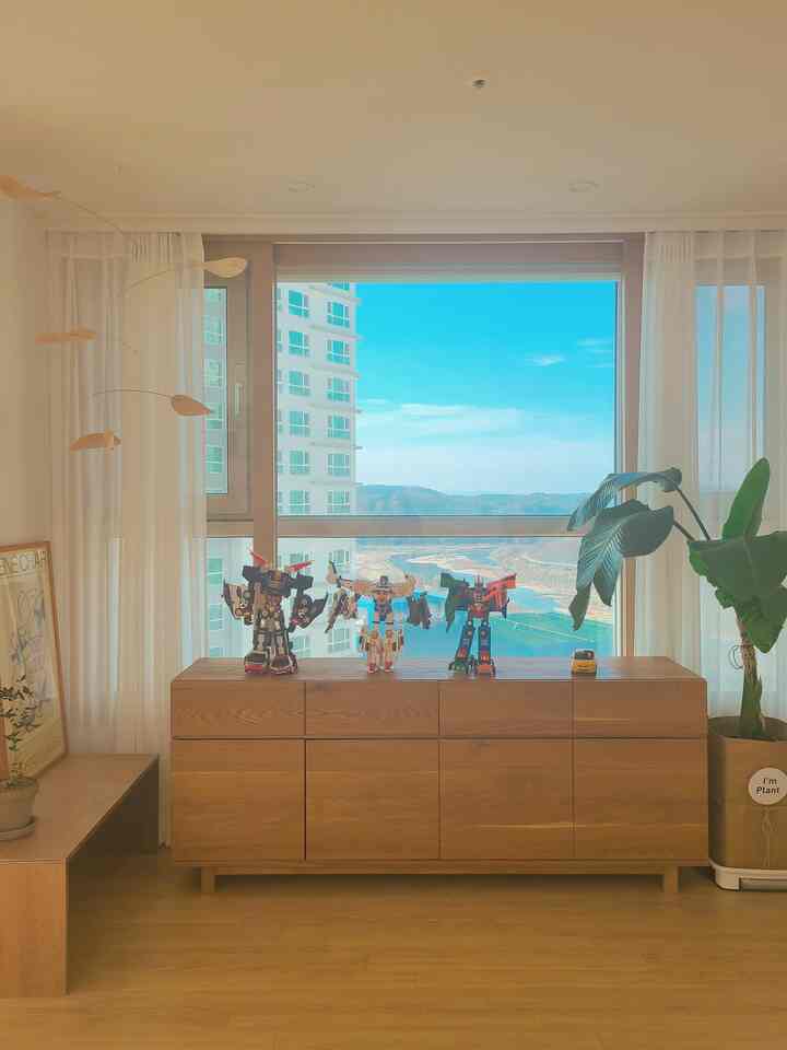 Bright living room with wood tone flooring and sideboard, featuring white chiffon curtains