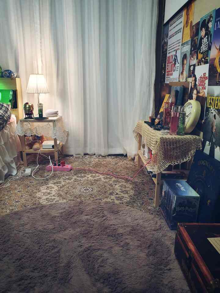ナチュラルカラーとヴィンテージスタイルの小さな部屋で、白いカーテンとカラフルな映画ポスター、ラグ、サイドテーブルが配置された雰囲気のあるインテリア