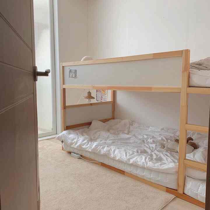 温かみのあるホワイトとナチュラルウッド調の子供部屋、木製二段ベッドとクリーム色のラグが配置されたシンプルで雰囲気のあるインテリア