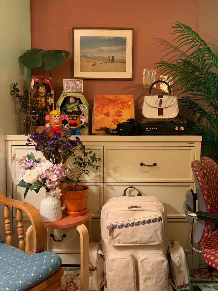 Cozy vintage-style room featuring warm orange walls, wood-toned furniture, stool, plants, and picture frame decor