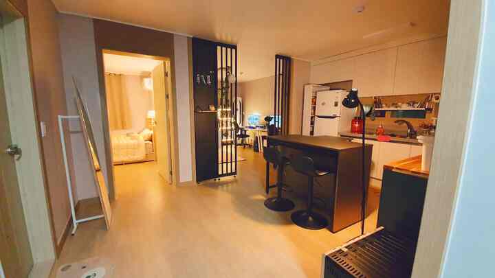 暖かいトーンの二人暮らしのキッチンとリビング、黒のアイランドバーテーブルと全身鏡、間仕切りが配置されたモダンなインテリア