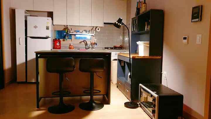 ダークブラウンと白を基調としたモダンなキッチン、移動可能な隙間収納とバースツールが配置された印象的な空間