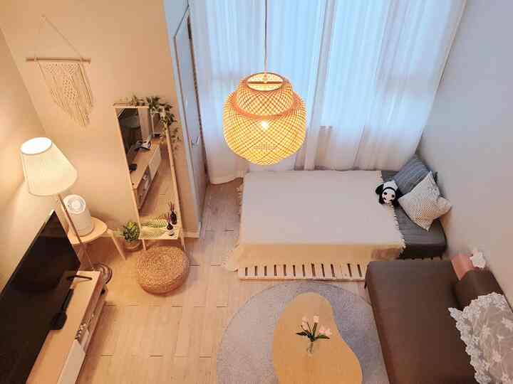 Soft natural tone studio living room with wooden flooring, rattan pendant lamp, and harmonious simple sofa and bed setup