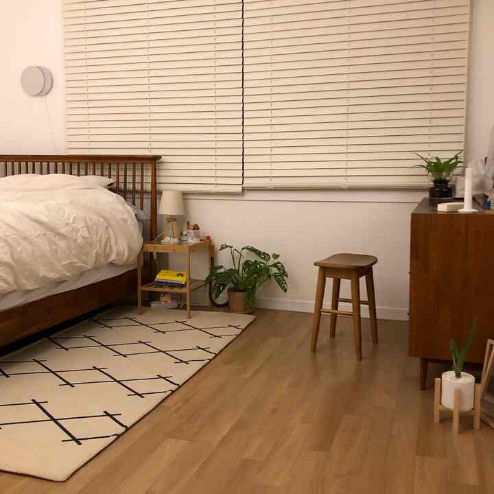 A bedroom with white and wood tones featuring a wooden bed frame, nightstand, rug, and plants, creating a calm natural atmosphere