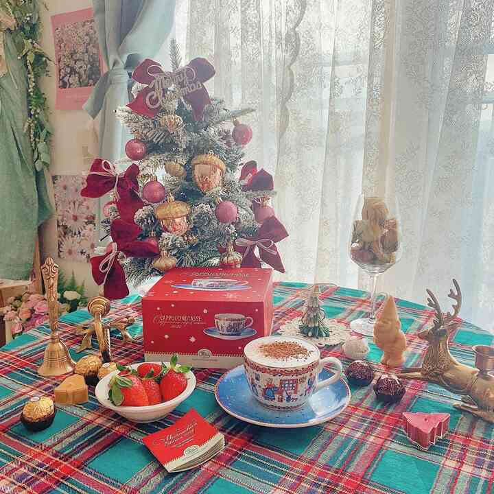 白とゴールドのレースカーテンを背景に、クリスマスツリーと赤緑のチェック柄テーブルクロスが配置された雰囲気のあるおうちカフェ空間