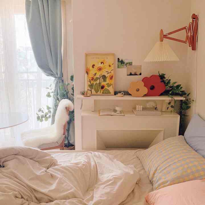 柔らかなブルーのカーテンとベージュの寝具が調和する落ち着いた寝室、暖炉風の棚と植物が配置された自然な雰囲気のインテリア