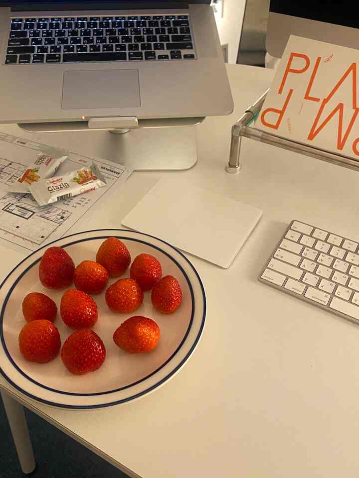 White-toned home office featuring a laptop, Magic Trackpad, and plate of strawberries on a clean desk setup