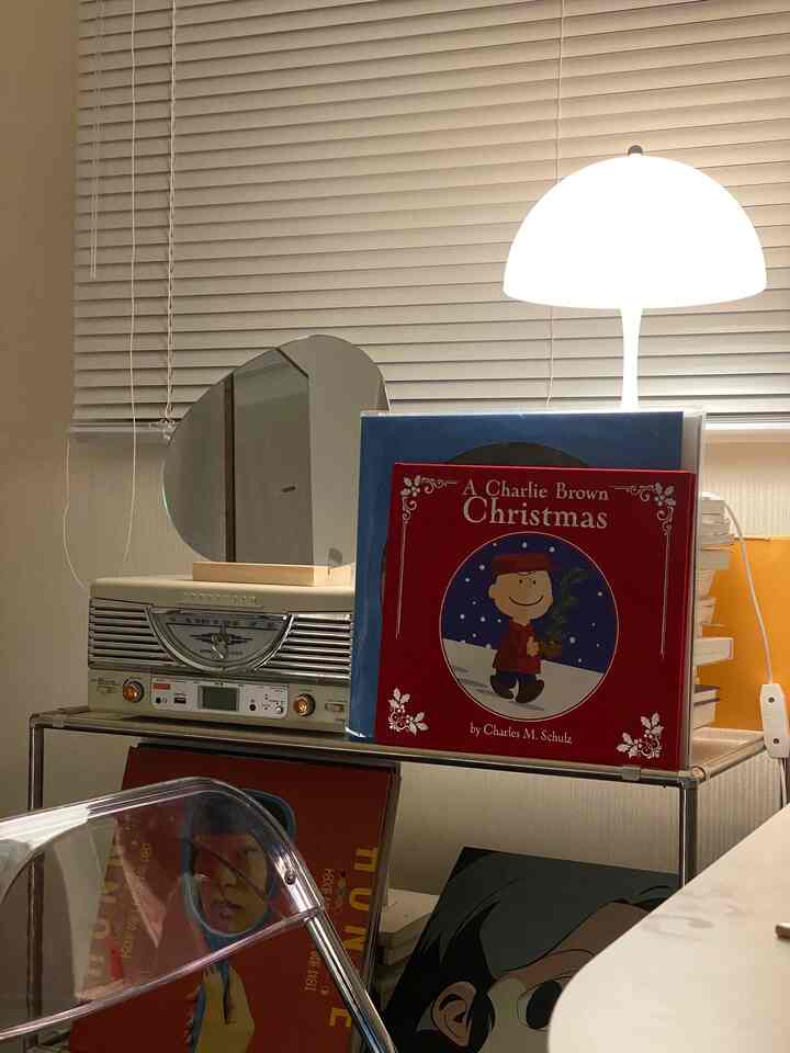 白とグレー調のワークスペース、パンテラミニのテーブルランプとモジュール棚、LPレコードとレトロラジオが配置された落ち着いた雰囲気のインテリア