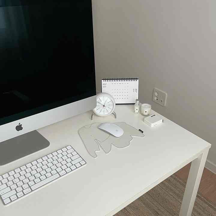 Bright white tone single-person home office space featuring a minimal desk, computer, and analog clock arranged neatly.
