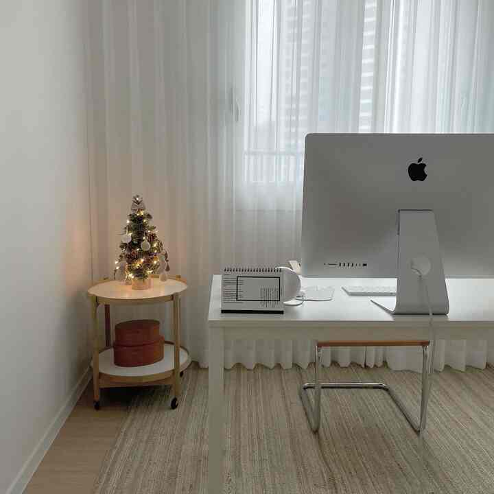 Small home office with white and natural tones, featuring a mini Christmas tree and simple furniture arrangement