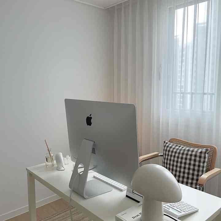 明るいホワイトトーンのホームオフィス、白いデスクとiMac、チェック柄クッションの木製アームチェアが配置されたミニマルなインテリア