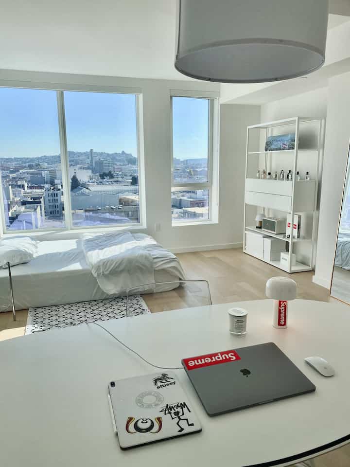 白を基調としたモダンな寝室、棚と大きな窓から見える都市の景色が特徴的なシンプルな一人暮らしの空間