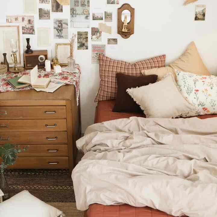 ベージュとナチュラルな色調の寝室、ヴィンテージのドレッサーと多くのクッションが配置された温かみのある居心地の良いインテリア