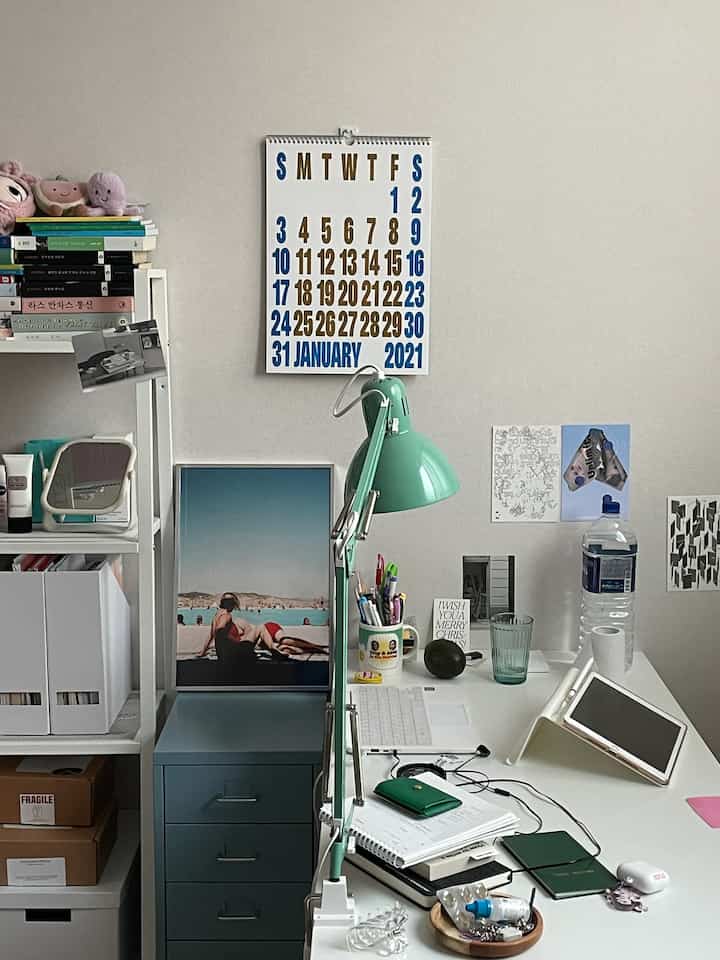 A white and mint-toned home office space featuring a white desk with a laptop and tablet, and a prominent wall calendar.