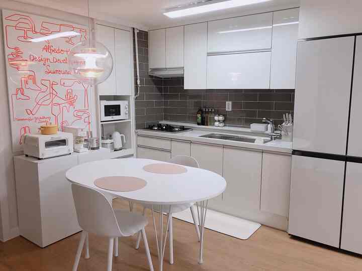 Modern kitchen space blending white and natural wood tones, featuring a simple dining table and organized storage with clean interiors