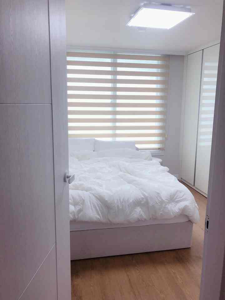A simple and modern bedroom with white and natural wood tones, featuring a duvet cover and soft combi roller blind.