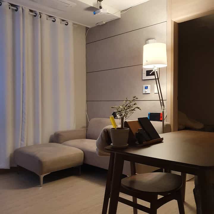 Beige-toned small living room featuring sofa, floor lamp, wooden table, and plant with a modern interior vibe