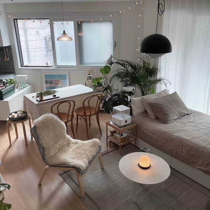 Warm beige-toned studio living room with bed, dining table, and pendant lights creating a cozy natural modern interior