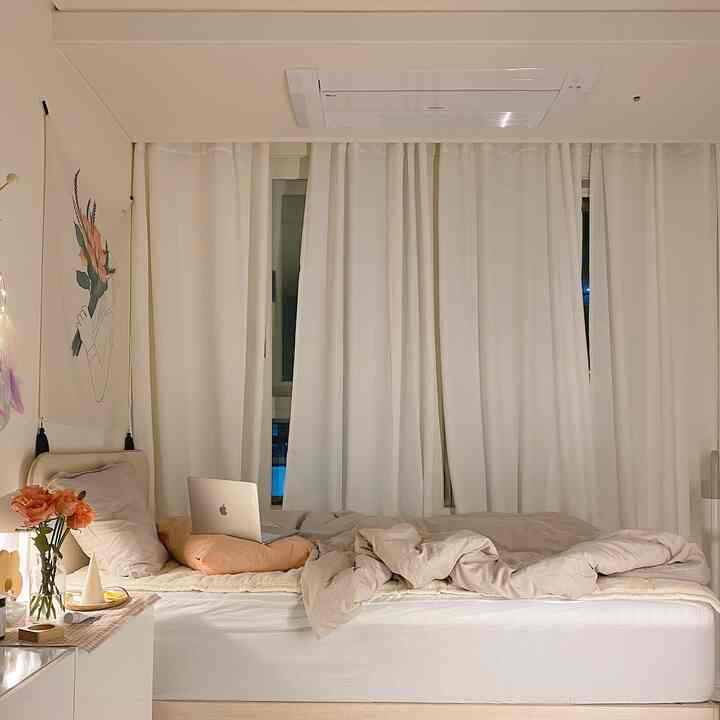 白とベージュの落ち着いた色調の寝室で、ベッドと遮光カーテンが配置されたシンプルでナチュラルな印象的な空間