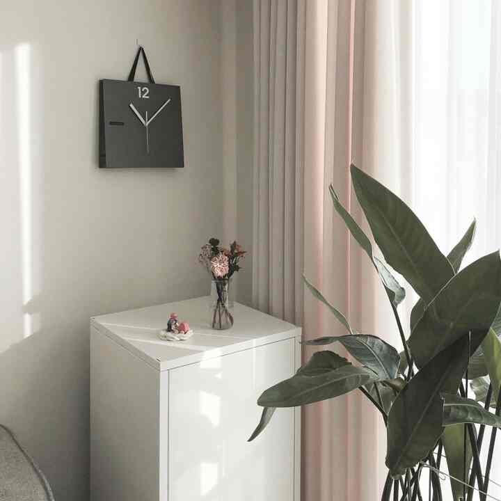 白とナチュラルトーンのリビング収納キャビネットと花瓶、ピンク色のカーテンと緑の植物が配置された落ち着いた雰囲気のインテリア