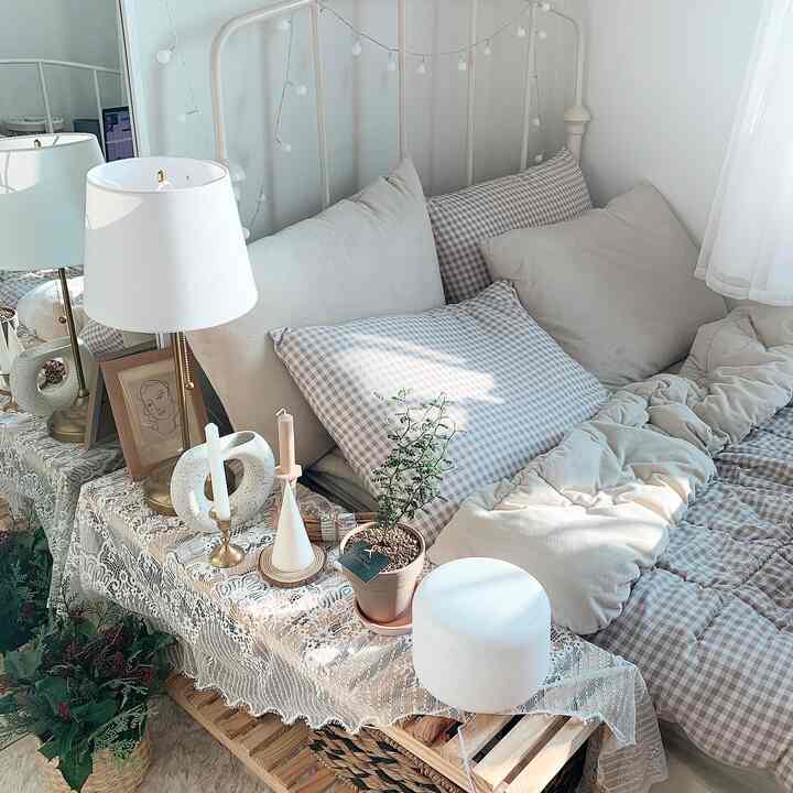 Bright white and beige bedroom featuring an IKEA bed, nightstand with table lamp, lace curtains providing a cozy and natural atmosphere