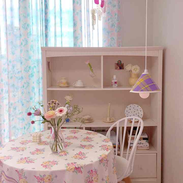 A living room space blending pink and white tones, featuring a floral round table and bookshelf creating a cozy atmosphere.