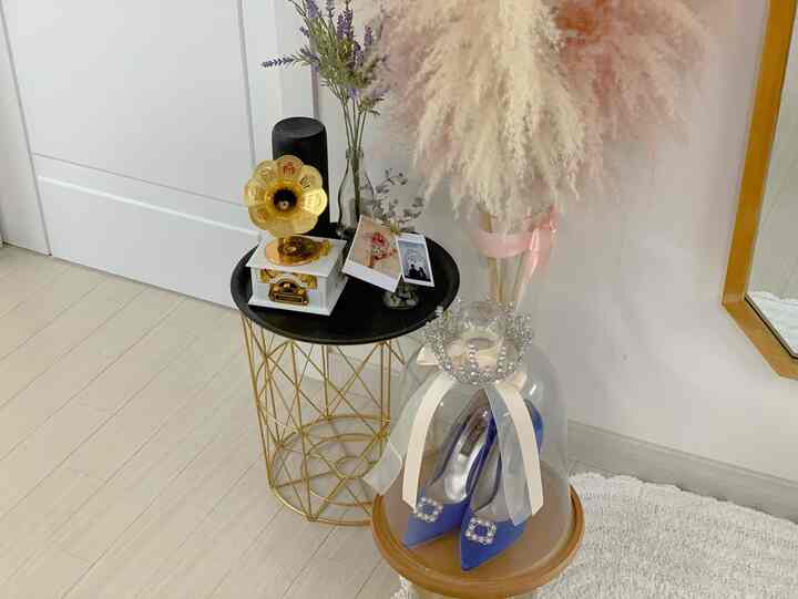 Natural interior with white walls and light wooden floor featuring a gold wire table holding a vintage music box and lavender bush, below which sit jeweled blue wedding shoes and a tiara