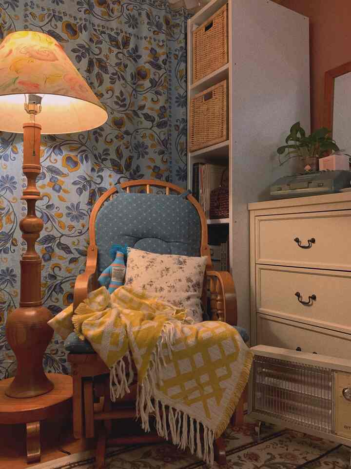 Warm wood-tone study featuring a rocking chair with cushions and blanket, electric heater, and soft yellow lighting creating a cozy atmosphere