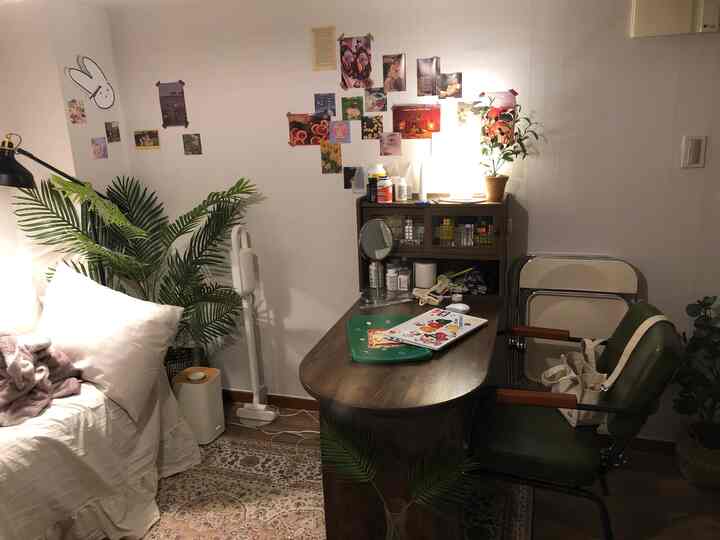 白い壁と木目調の机が調和するワンルームの書斎空間、オリーブグリーンの椅子と植物が配置された落ち着いたホームオフィスの雰囲気