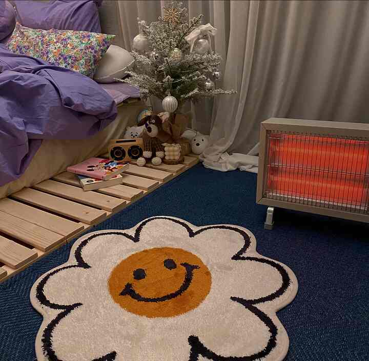Cozy bedroom with purple bedding and white curtains, featuring mini Christmas tree and smiley flower rug