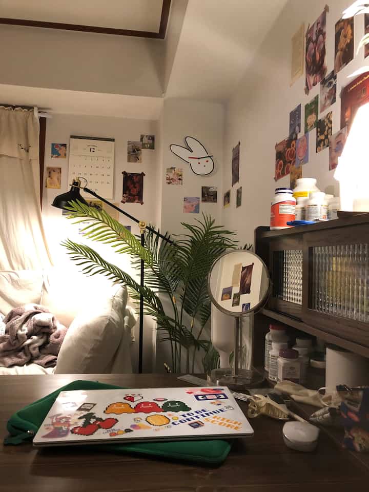 Natural-colored small room featuring a sofa bed, desk, table lamp, and plant, creating a cozy home office atmosphere