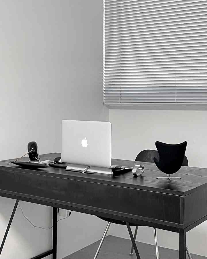Monotone minimal home office space featuring a sleek desk with laptop and blinds creating a modern atmosphere