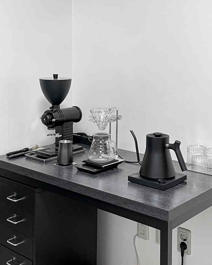 Monotone modern coffee bar space featuring black dresser and desk with coffee equipment neatly arranged