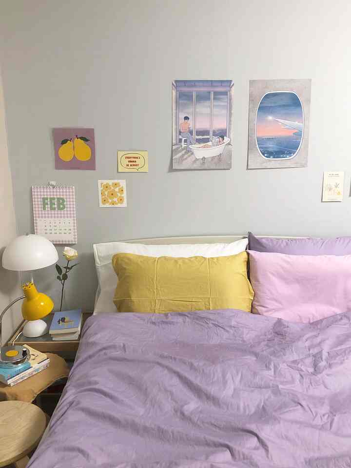 Lavender and yellow toned bedroom featuring bed with pillows and artistic posters on wall creating a hotel-like atmosphere