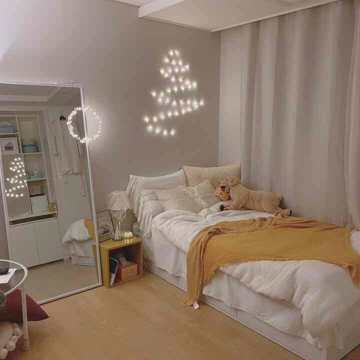 黄色とベージュのトーンの寝室、クリスマスの壁ツリーLEDライトとぬいぐるみの犬が温かみのある雰囲気を演出するインテリア