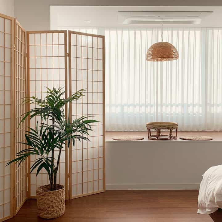 白と茶色のトーンの寝室、ラタンの間仕切りとペンダントライトが配置された自然で温かみのあるインテリア