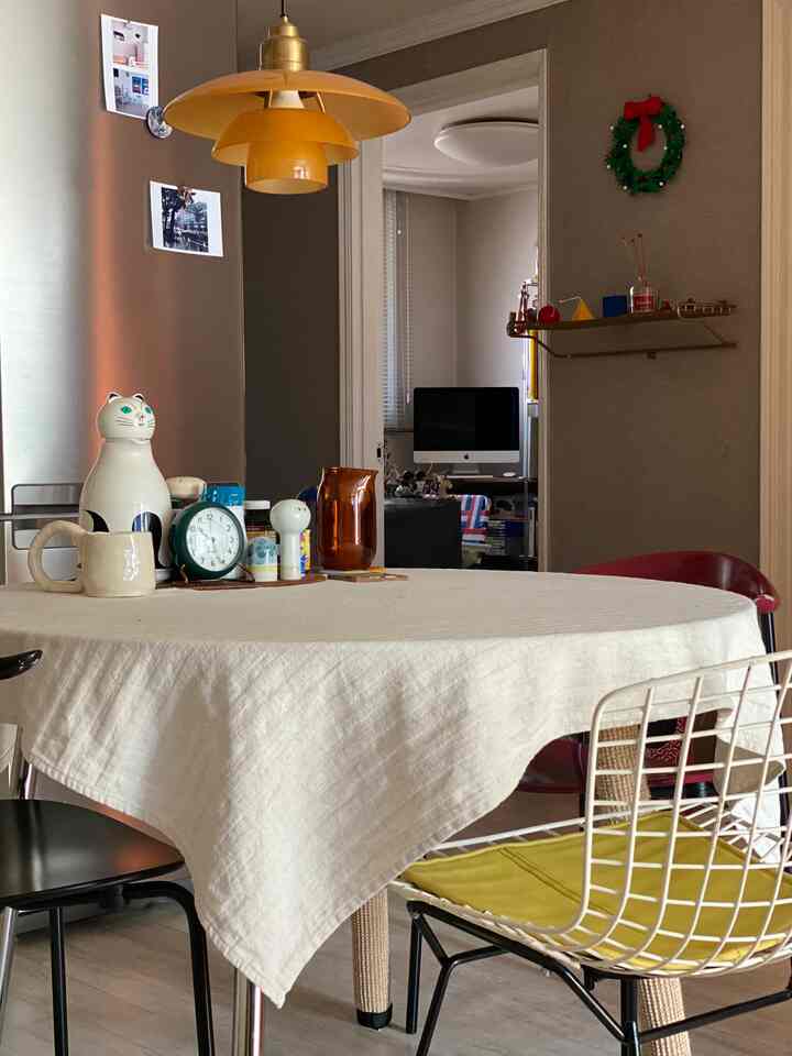 ナチュラルな色調のダイニング空間、中央にベージュのテーブルクロスをかけた丸テーブルと多様な椅子、黄色いペンダントライトのある雰囲気のあるインテリア