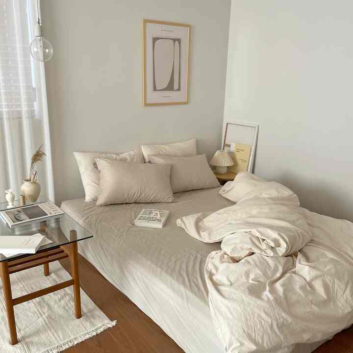 柔らかなベージュ色調の寝室、ベッドと枕、木製テーブルが調和したナチュラルなインテリア