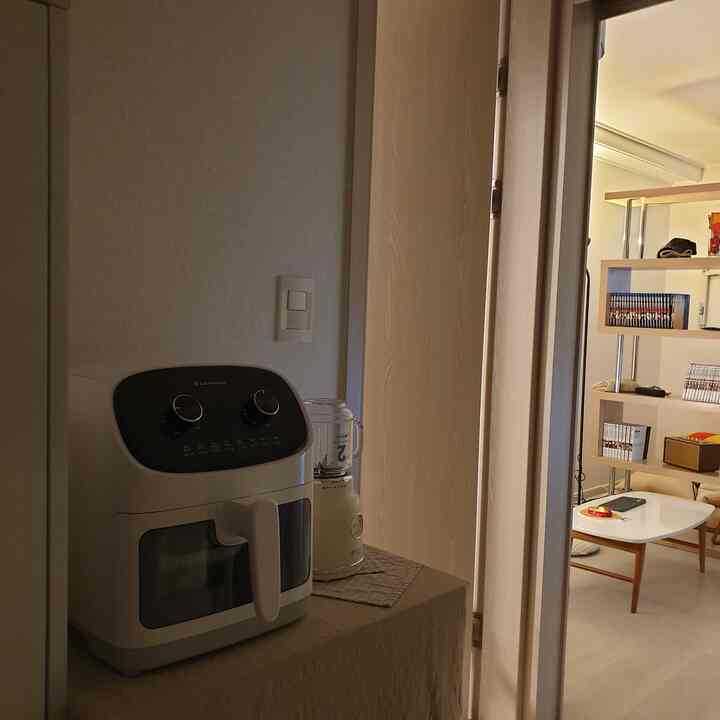 ナチュラルな木目調とベージュのテーブルクロスが調和した玄関の棚にエアフライヤーやミキサー、電子レンジが置かれた居心地の良いワンルームの空間