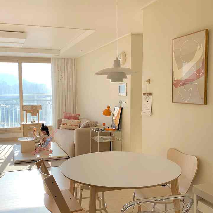 Natural-tone kitchen and living area featuring a round dining table, sofa, and a child’s play space with warm atmosphere
