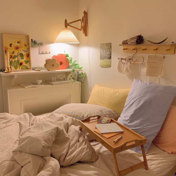 居心地の良いナチュラルトーンの寝室、木製の折りたたみベッドテーブルと壁付けランプが配置された暖かみのあるインテリア