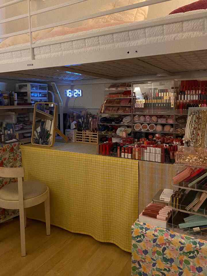 Compact small room featuring a yellow checkered tablecloth desk under a loft bed, with vanity and a digital clock creating a cozy atmosphere